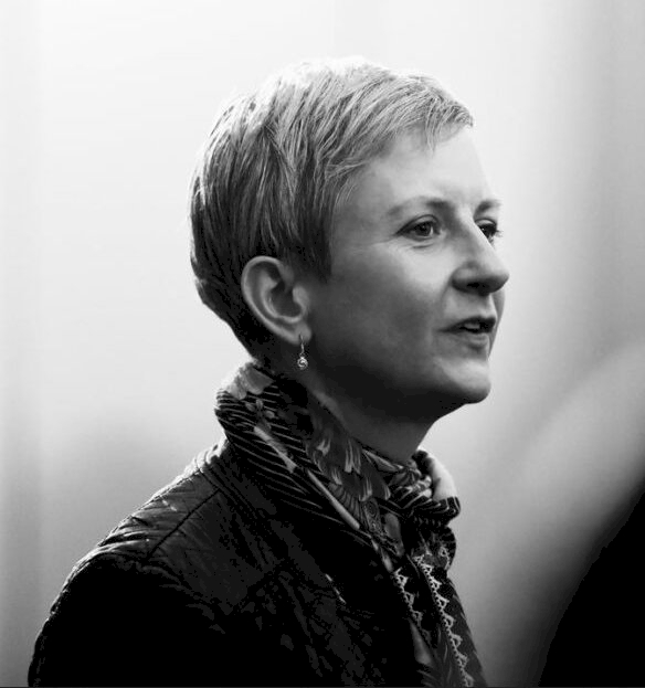 A monochrome photo of a short-haired woman wearing a scarf, in profile and looking to the right.